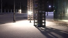 Snow night park. Snow is falling on empty city park. A lonely snow-covered bench stands near sea. Christmas Winter New Year Scenery background. Frosty winter in the city after snowfall