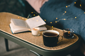 Wall Mural - Cup of tea with scented candle with stack of paper book over glow lights in cozy living room closeup. Winter holiday season. Aromatherapy.