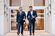 Businessmen walk in the street. Two businessmen walking and talking at office building. Two american businessmen in suits walk outdoors in the city and discuss business. Successful business concept.