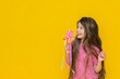 © Юлия Дьякова - The surprised girl eats a lollipop. A model with a fashionable hairstyle and beautiful makeup, holding a pink sweet lollipop on a stick, highlighted on a yellow background. space for copying .