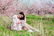 © dmitriisimakov - beautiful woman sitting by a tree in pink flowers nature parks walk peach garden