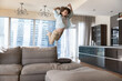 Excited crazy boy kid jumping on big sofa, throwing body on soft couch with wild scream, flying in air, playing game, enjoying activities, leisure time, playtime at home, having fun