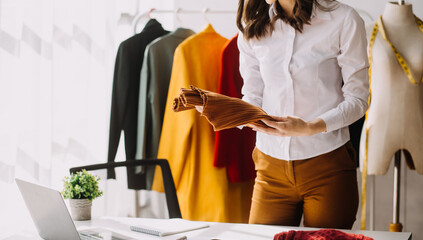 Fashion designer l young asian woman working using laptop, tablet and smiling while standing in workshop Responding on business