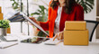 © ARMMY PICCA - Startup small business SME, Entrepreneur owner woman using smartphone or tablet taking receive and checking online purchase shopping order to preparing pack product box. at home office