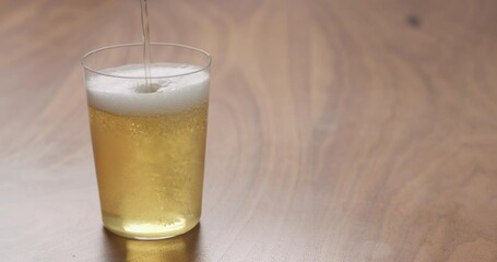 Wall Mural - Slow motion pour apple cider in thin glass on wood surface with copy space