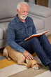 © Space_Cat - Senior man sits on the floor with his dog and reading a book. Elderly man with enjoying his happy retirement at home