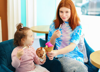 Portrait of two young sisters holding hands and eating ice cream in cafe.