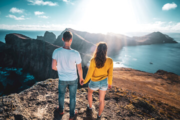 Wall Mural - Back view of a touist couple holding hands, enjoying the coastal landscape of Madeira Island in the Atlantic Ocean in the morning. São Lourenço, Madeira Island, Portugal, Europe.