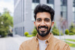 © Liubomir - Close up photo portrait of young Hindu student, man smiling and looking at camera, businessman outside office building wearing shirt.