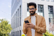 © Liubomir - Successful Indian young businessman outside office building walking in daytime, man holding phone in hands, businessman dialing, browsing online pages, programmer engineer in glasses.