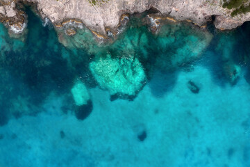 Wall Mural - Summer holiday background. Top view of seascape with beautiful stone cliff and clear blue water on a sunny summer day. Sea coast, aerial drone shot. Travel concept