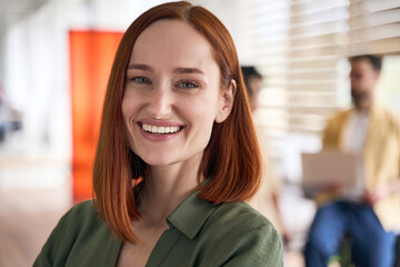 Wall Mural - Closeup portrait of attractive smiling red haired student standing in university campus, education concept. Confident businesswoman, successful manager looking at camera