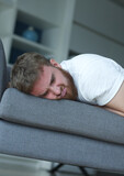 Fototapeta  - Exhausted young man fell asleep on comfortable couch in modern living room, having no energy after hard working day. Tired depressed unmotivated european guy napping on sofa at home, fatigue concept.