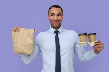 Sticker - Happy young intern holding takeaway cups with hot drink and paper bag on lilac background