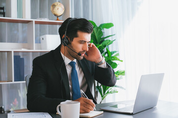 Male call center operator or telesales representative siting at his office desk wearing headset and engaged in conversation with client providing customer service support or making a sale. fervent