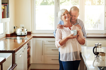 Wall Mural - Hugging, coffee or old couple laughing in kitchen at home bonding or enjoying quality time together. Embrace, retirement or happy mature man talking, relaxing or drinking tea with funny senior woman