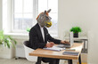 © Studio Romantic - Funny business man and company employee wearing suit and animal donkey mask sitting at the desk on his workplace and working on a laptop in office. Entertainment, fun and fools day concept.