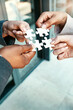 © L De Bruin/peopleimages.com - Closeup, hands and puzzle with collaboration, group and teamwork with partnership, planning and brainstorming. Zoom, staff and team with ideas, jigsaw pieces and cooperation with support and solution