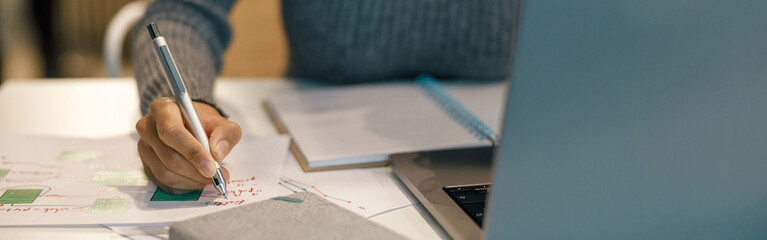 close up of woman freelancer working laptop and making notes while sitting near windows in cozy cafe