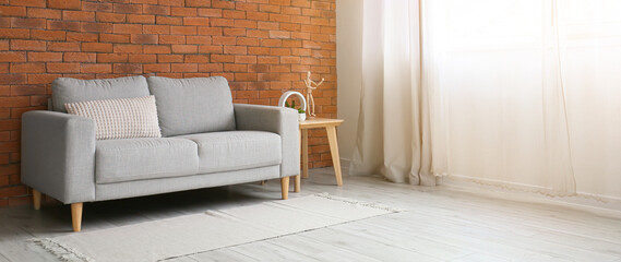 Grey sofa near brick wall in living room. Banner for design