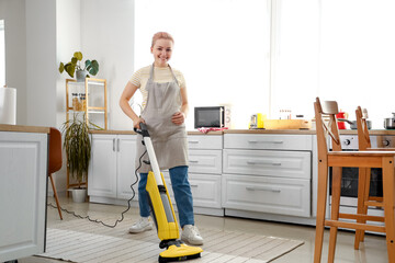 Canvas Print - Young woman hoovering carpet in kitchen