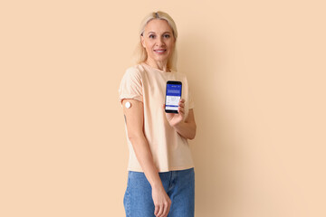 Sticker - Mature diabetic woman with mobile phone measuring blood sugar level on beige background