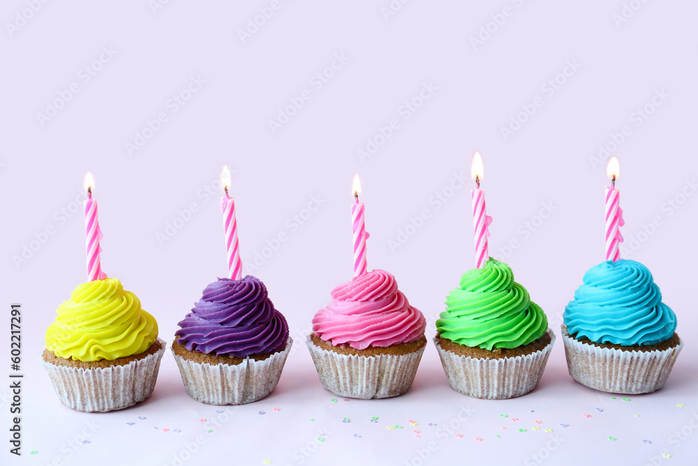 Tasty cupcakes with birthday candles on lilac background