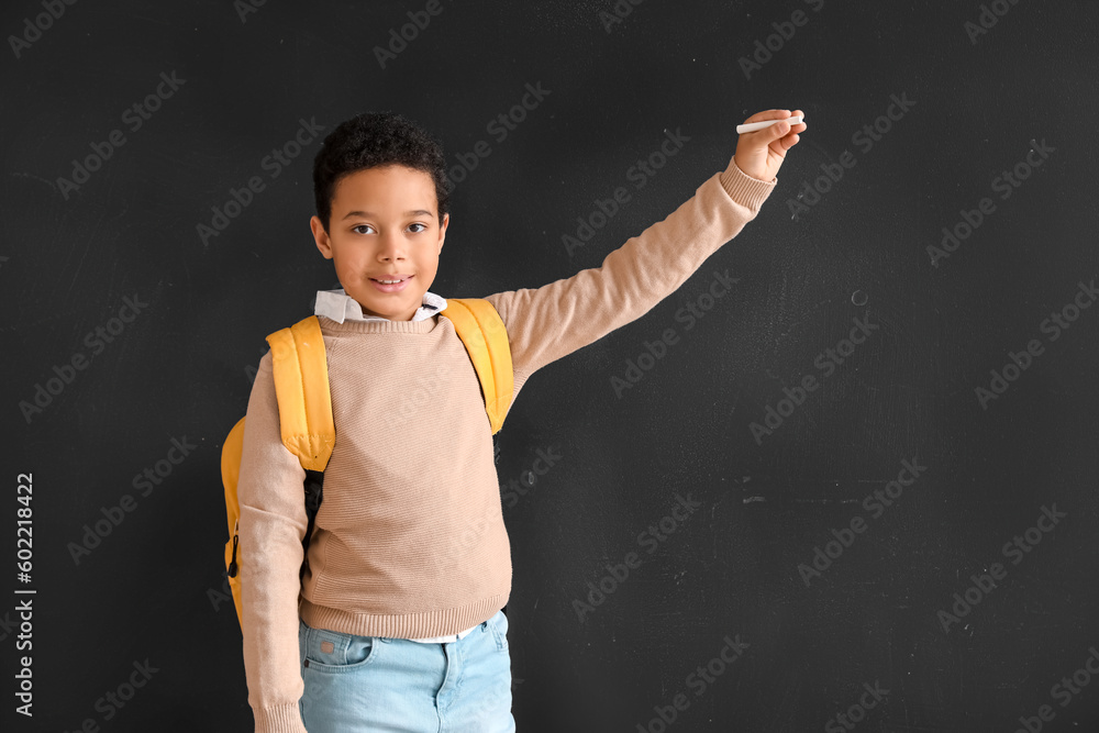 Little African-American boy with chalk piece drawing on blackboard. Children's Day celebration