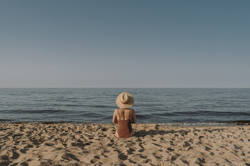 Pretty woman sitting on beach sand and watching at sea and sky. Minimal summer vacation concept. Chilling, relaxing near ocean inspirational composition