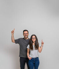 Wall Mural - Smiling young couple pointing up at copy space for marketing against background. Happy man and woman wearing eyeglasses showing empty space for advertisement