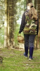 Wall Mural - A young woman in a camouflage jacket walks through the woods with a basket. Looking for mushrooms. Vertical video.