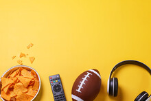TV Remote, A Bowl Of Chips And A Headphones On A Yellow Background. American Football And Super Bowl Concept.