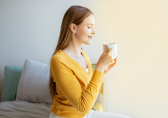 Wall Mural - Young Woman Smelling Aroma Of Coffee Holding Cup In Bedroom