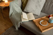 © Prostock-studio - Book, tray with food and coffee cup on sofa in living room interior at evening, top view