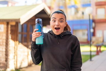 Wall Mural - Young pretty sport woman with a bottle of water at outdoors with surprise and shocked facial expression