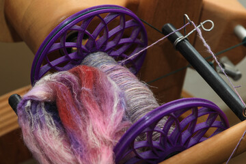 Closeup detail of a bobbin full of colourful organic natural handspun and handdyed merino sheep wool yarn , spun on a traditional spinning wheel.	