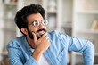 Portrait Of Pensive Smiling Indian Man Wearing Eyeglasses Posing In Home Interior