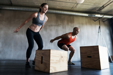 Wall Mural - Gym, couple and exercise with box jump for training, workout and intense cardio on wall background. Health, fitness and people at a sports center for wellness, performance and endurance challenge