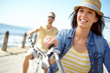 Bike, Cycling And Couple With A Travel Woman On Summer Vacation Or Holiday Riding On The Promenade By The Beach. Freedom, Date And Romance With A Girlfriend Outdoor For A Ride On The Coast