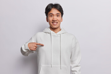 Are you talking about me. Cheerful Asian man points at himself shows blank copy space on sweatshirt for your advertising content isolated over white background. People design and template concept