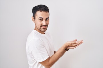 Sticker - Handsome hispanic man standing over white background pointing aside with hands open palms showing copy space, presenting advertisement smiling excited happy