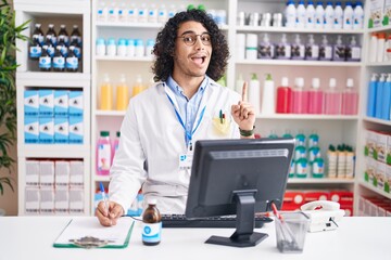 Wall Mural - Hispanic man with curly hair working at pharmacy drugstore pointing finger up with successful idea. exited and happy. number one.