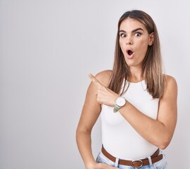 Canvas Print - Hispanic young woman standing over white background surprised pointing with finger to the side, open mouth amazed expression.