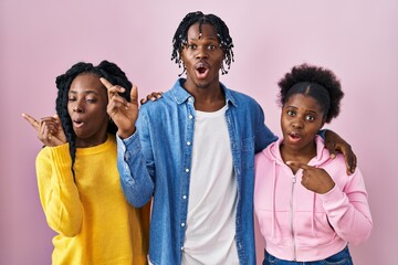 Poster - Group of three young black people standing together over pink background surprised pointing with finger to the side, open mouth amazed expression.