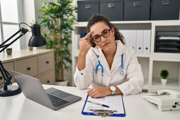 Poster - Young hispanic woman wearing doctor uniform and stethoscope pointing unhappy to pimple on forehead, ugly infection of blackhead. acne and skin problem