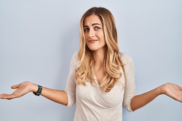 Wall Mural - Young blonde woman standing over isolated background clueless and confused with open arms, no idea concept.