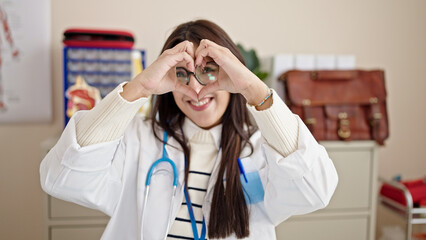 Canvas Print - Young beautiful hispanic woman doctor smiling doing heart gesture with hands at clinic