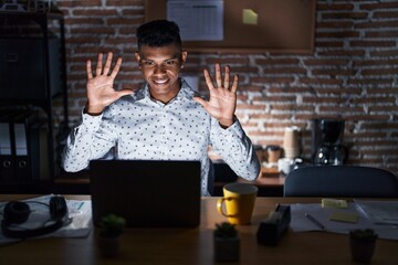 Sticker - Young hispanic man working at the office at night showing and pointing up with fingers number ten while smiling confident and happy.