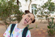 Portrait of a red haired crazy little girl with freckles laughing and sticking out her tongue in a park, concept of happiness and joy, carrying a backpack.