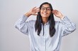 © Krakenimages.com - Young hispanic woman wearing glasses smiling pulling ears with fingers, funny gesture. audition problem